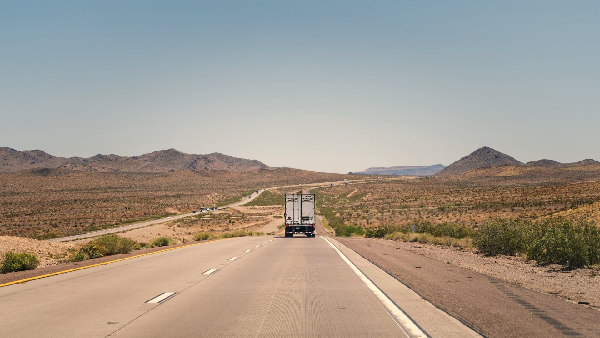 A truck on a straight desert highway with mountains on the horizon